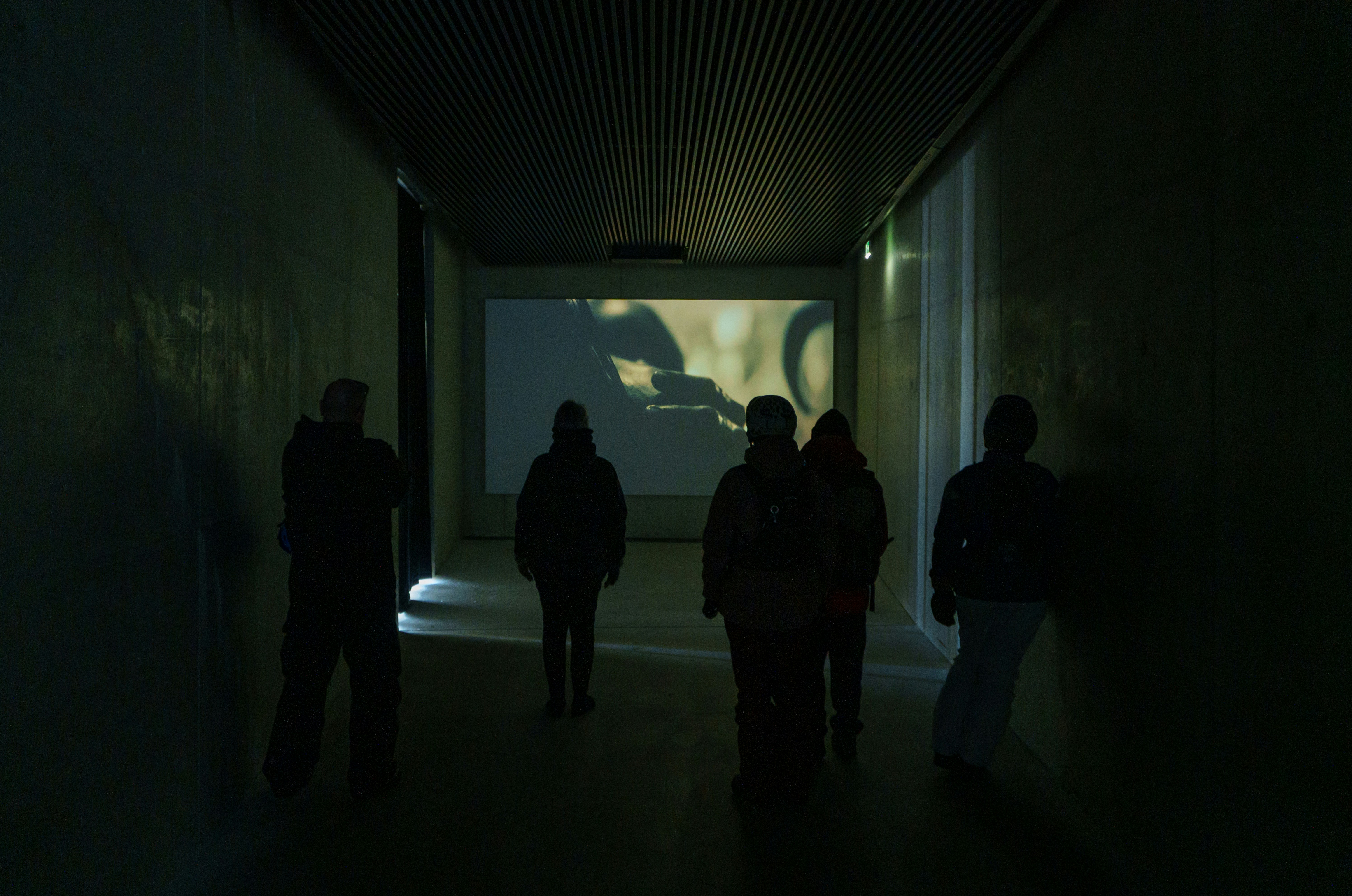 A video art gallery of patrons watching a film in a dark hallway.